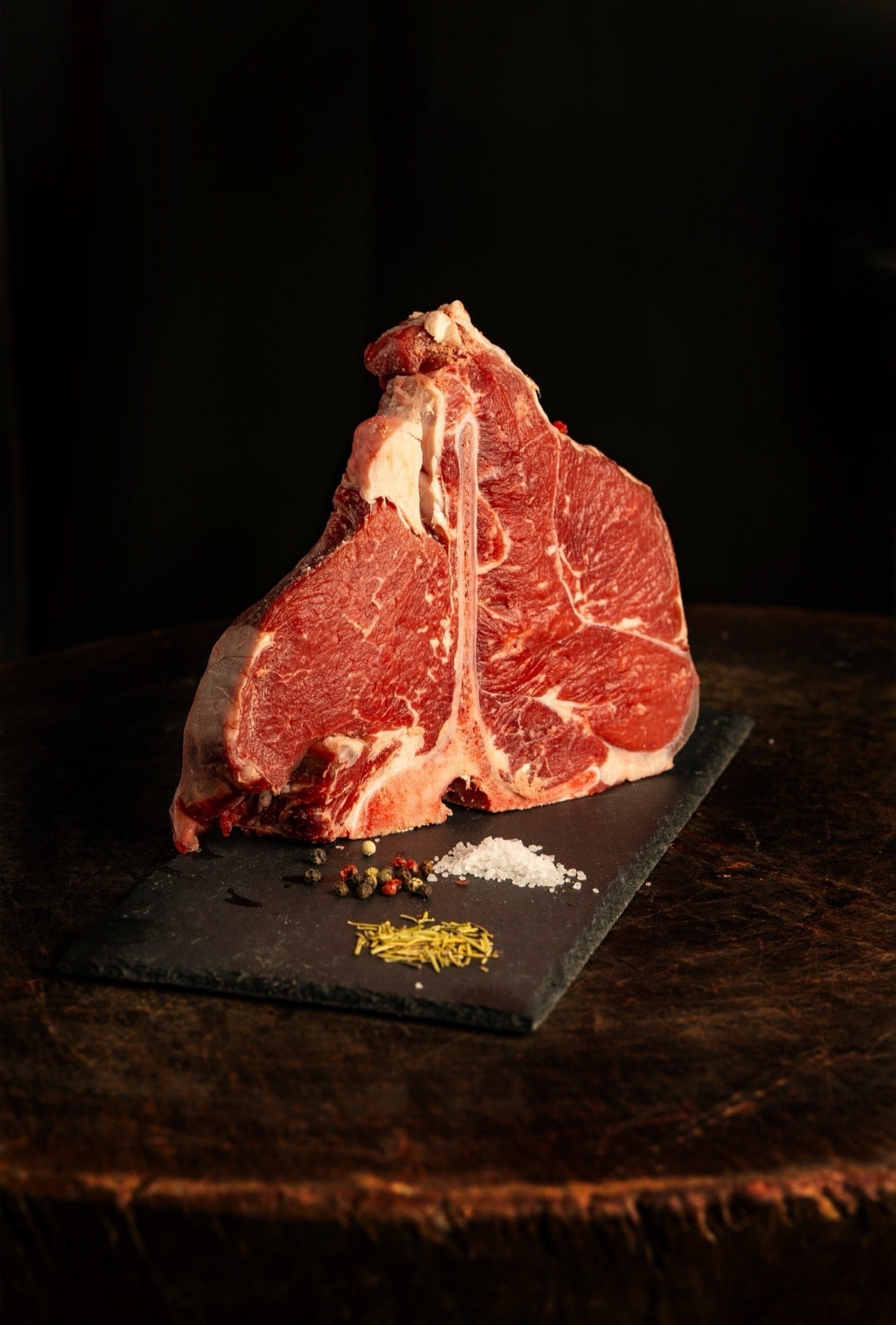 Φρέσκο T-bone μοσχαριού πάνω σε πλάκα, με αλάτι, πιπέρι και δεντρολίβανο